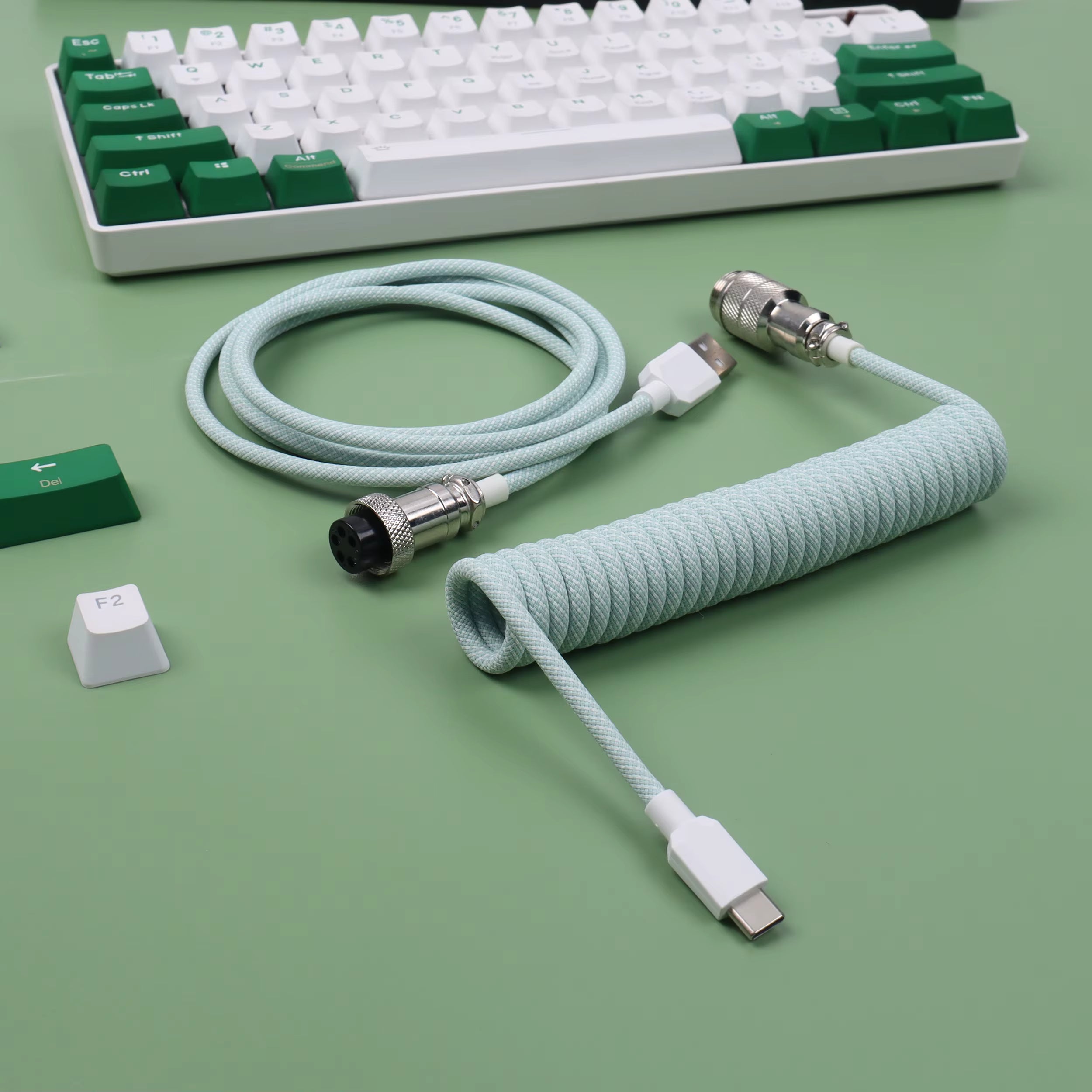 Mechanical keyboard with green and white keys, coiled cable on a green surface